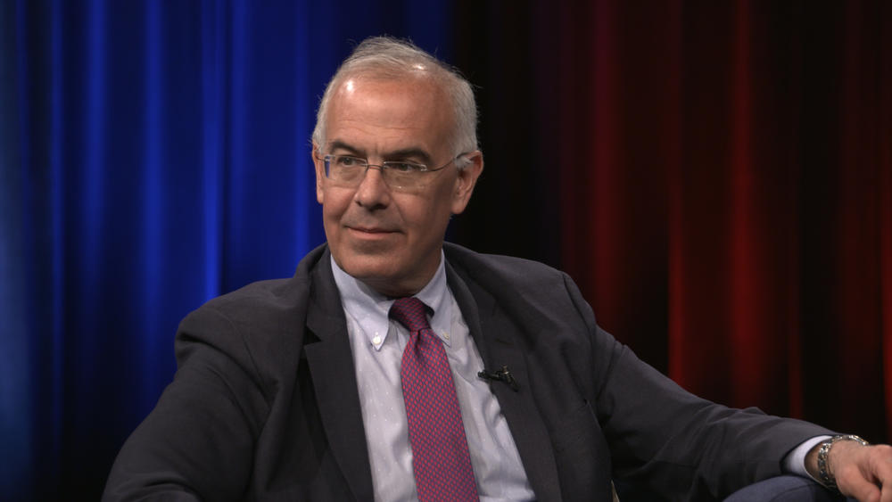 Man with gray hair and glasses, wearing a suit and tie, sitting and looking toward the interviewer.