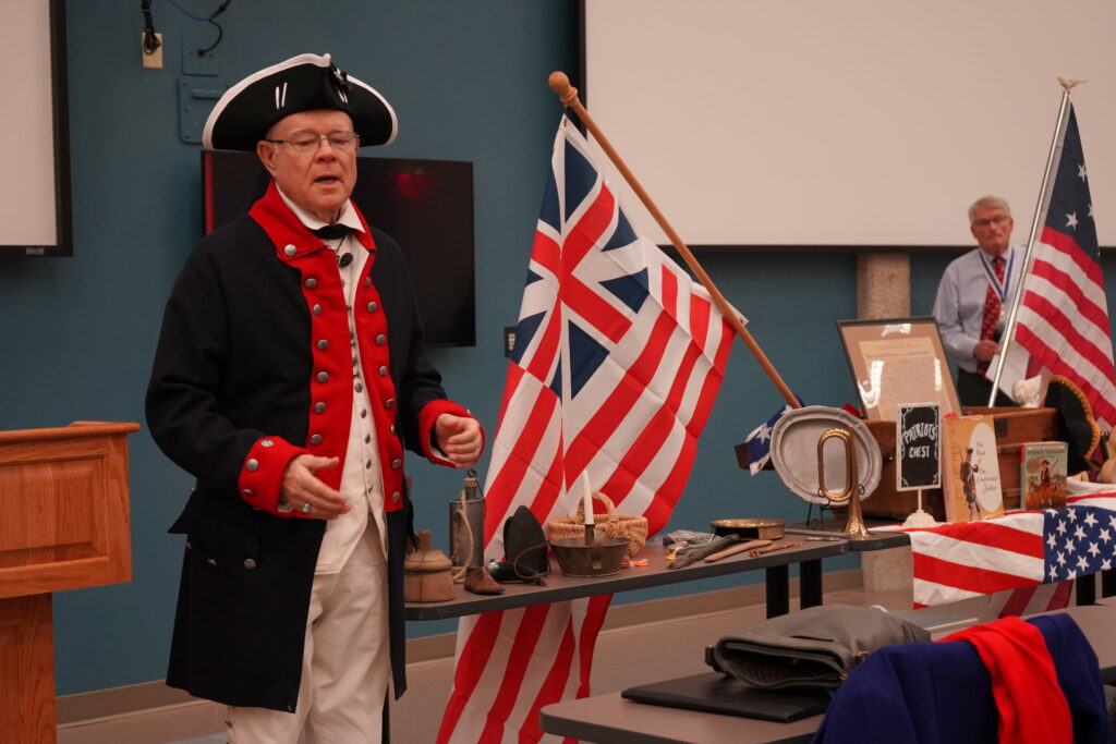 man dressed in colonial military uniform next to colonial era memorabilia